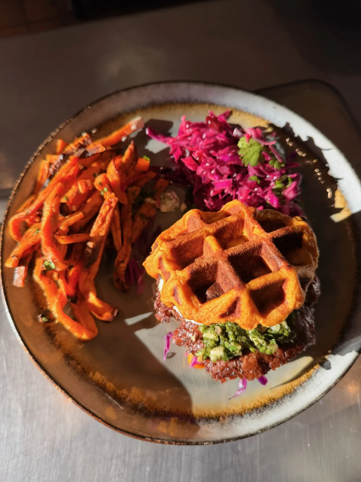 Top-down view of the sweet potato waffle-bun burger plate with chimichurri, Greek yogurt aioli, red cabbage salad, and sweet potato fries