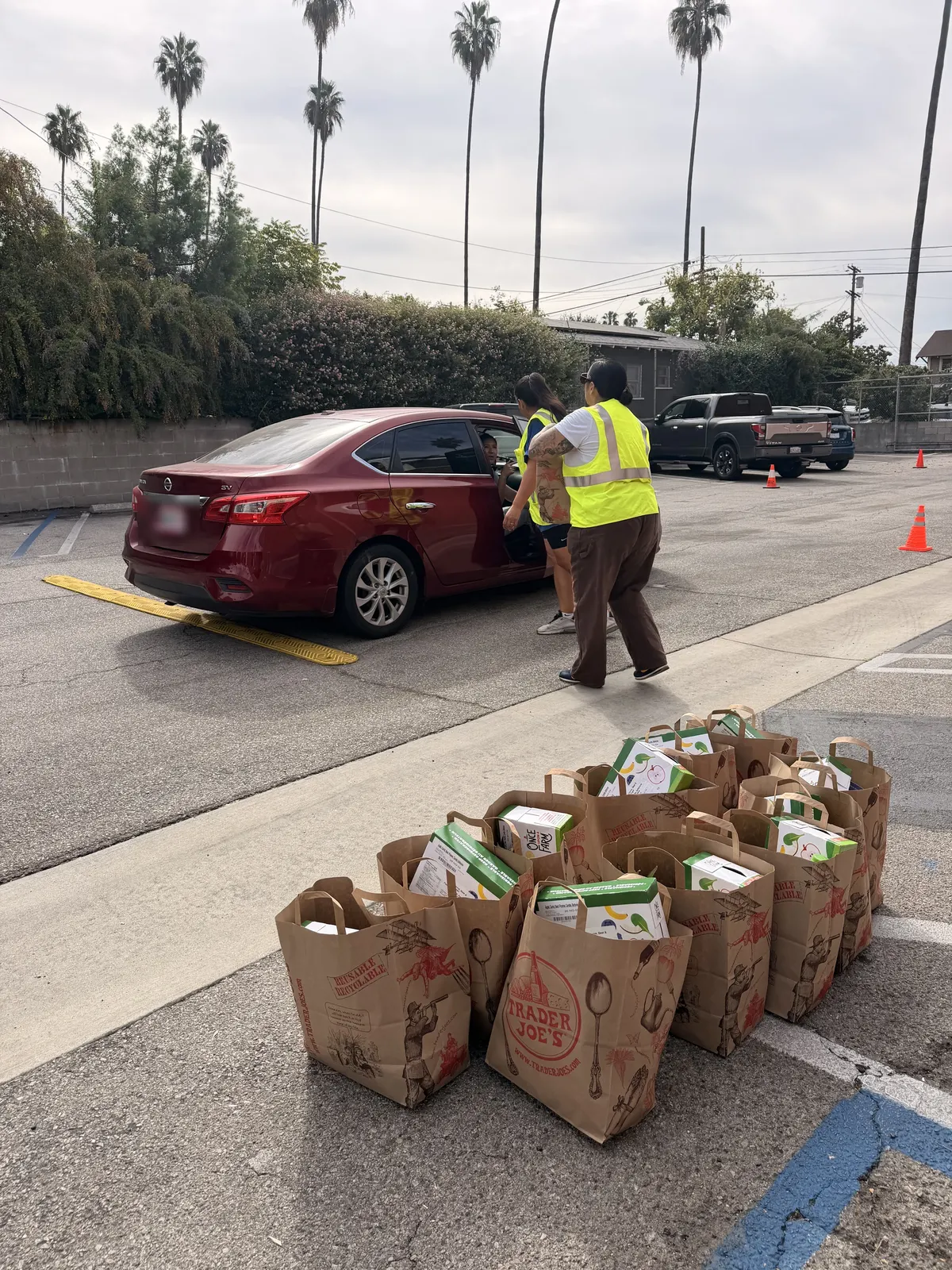 Volunteers in yellow vests loading bags of produce into a car at the drive through, with full bags lined up on the pavement