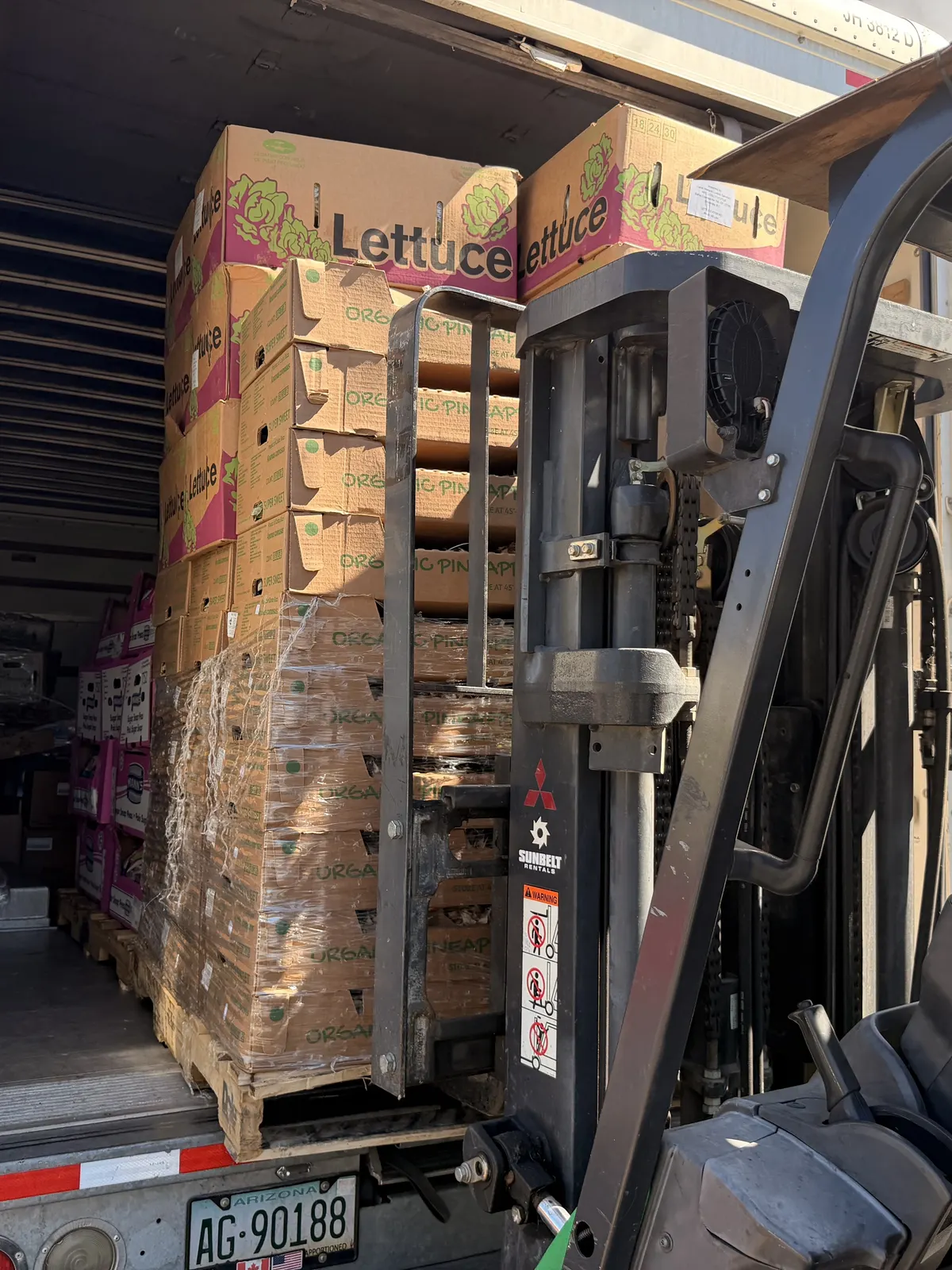 A forklift lifting a pallet of produce boxes into the back of a box truck