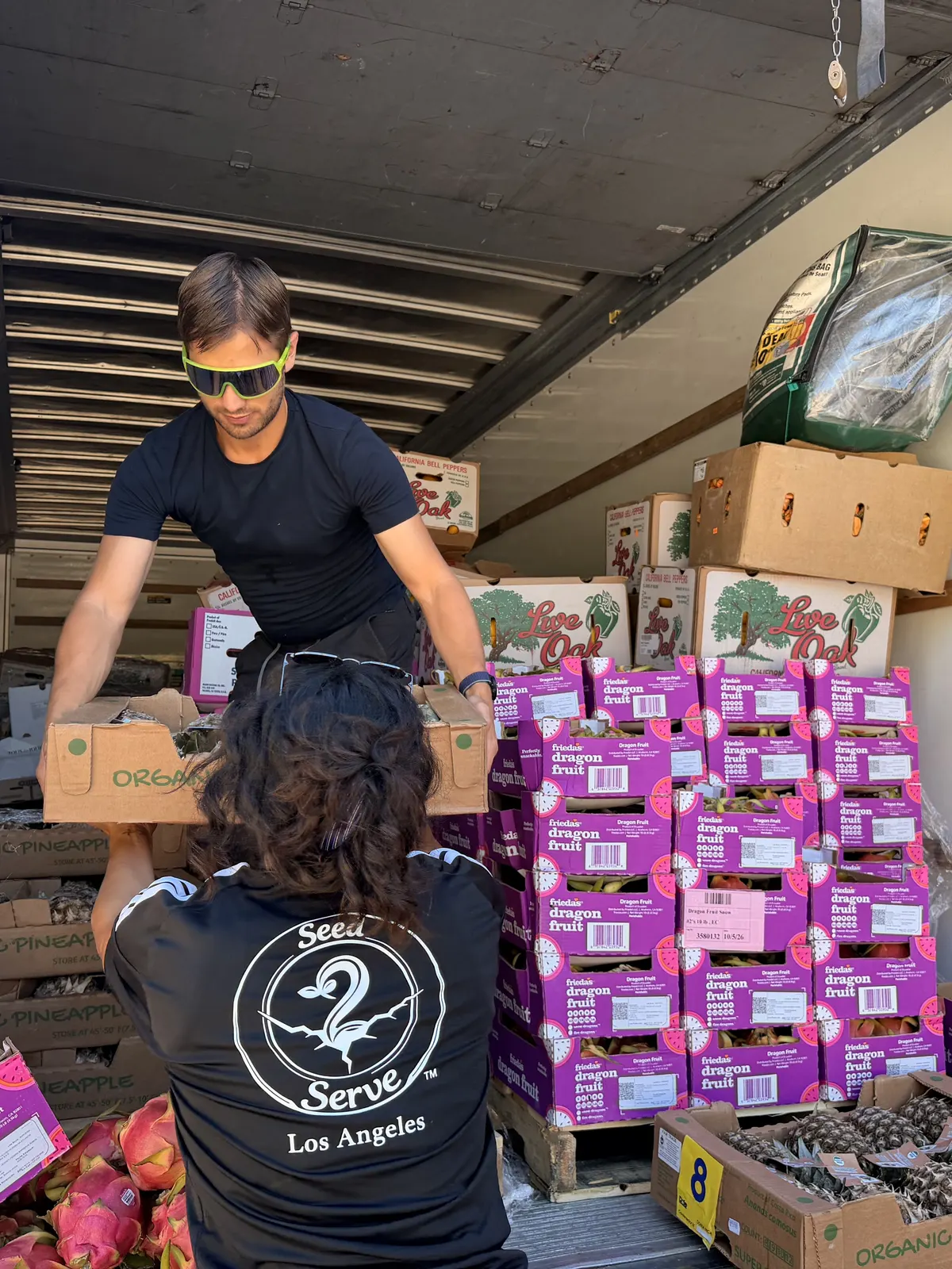 Two volunteers in Seed to Serve shirts unloading boxes of dragon fruit from the back of the truck