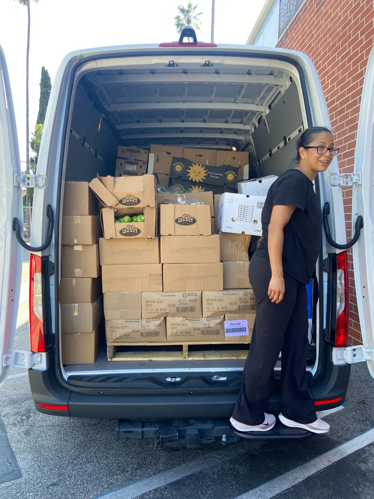 A volunteer standing beside a van stacked floor to ceiling with boxes of donated produce